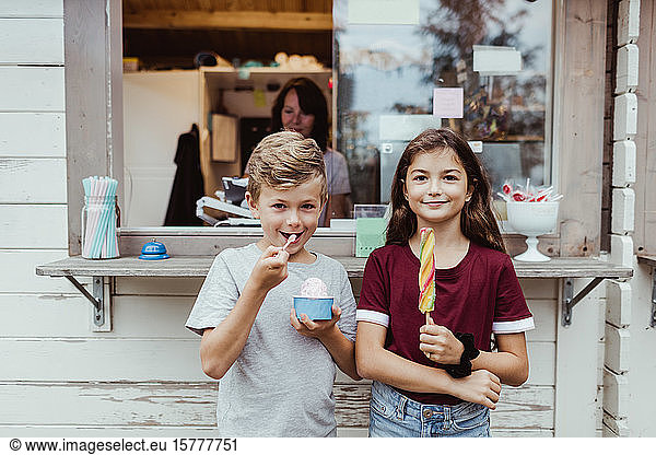 Portrait of sibling eating sweet food while standing against concession stand