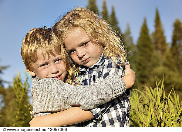 Portrait of siblings embracing at field on sunny day