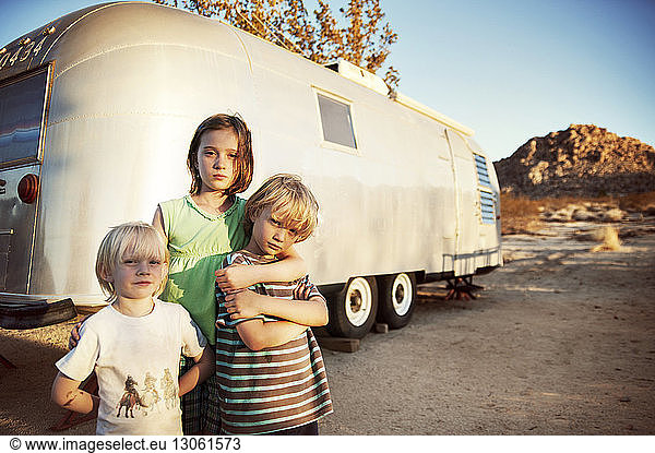 Portrait of siblings standing by camper van on sunny day