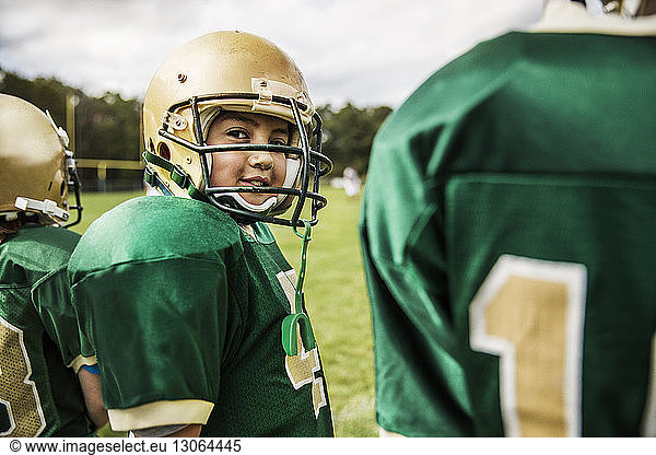 Portrait of smiling American football player with friends on field