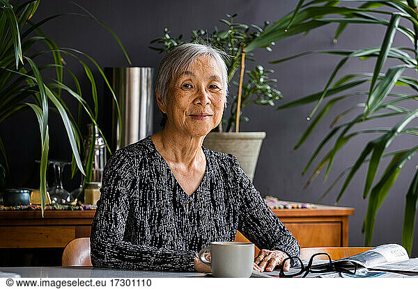 Portrait of smiling asian Senior Woman sitting at table at home