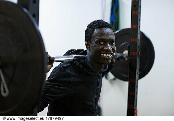 Portrait of smiling athlete carrying barbell on shoulder in gym