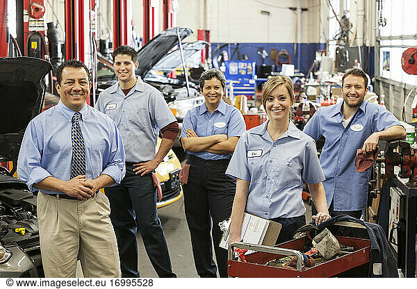Portrait of smiling auto repair shop team with Hispanic male owner