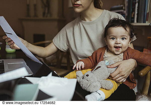 Portrait of smiling baby boy with businesswoman at home office