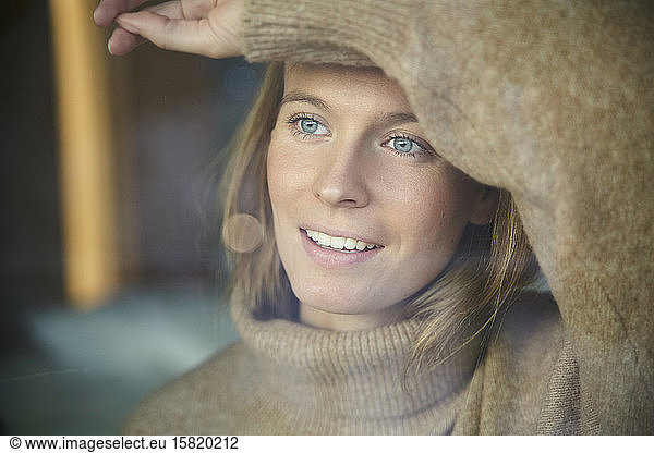 Portrait of smiling blond young woman behind windowpane