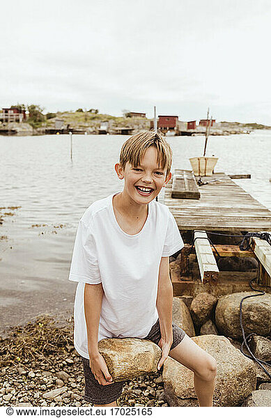 Portrait of smiling boy carrying rock against sea
