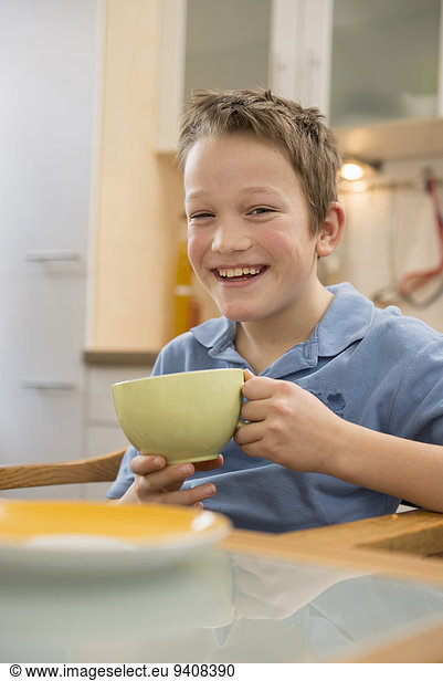 Portrait of smiling boy holding cup in kitchen