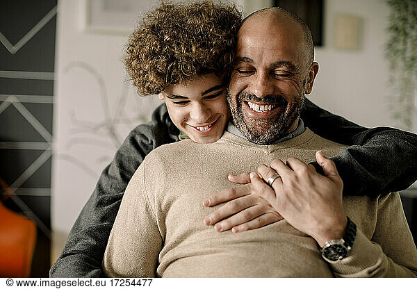 Portrait of smiling boy hugging cheerful father from behind