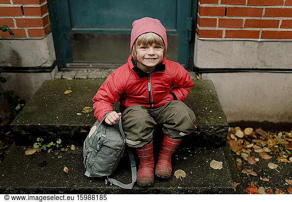 Portrait of smiling boy in warm clothing sitting on steps