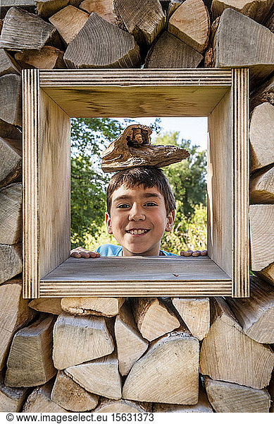 Portrait of smiling boy looking through window in logpile