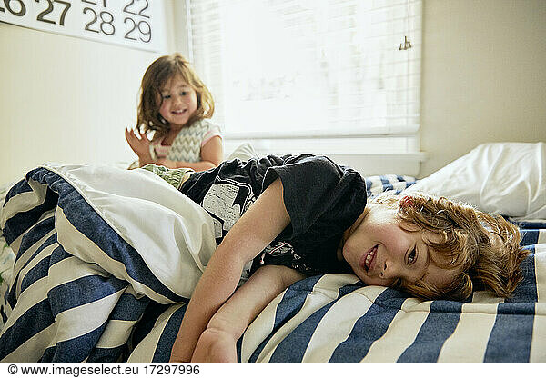 Portrait of smiling boy lying by sister on bed in bedroom at home