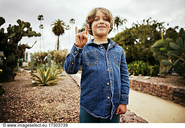Portrait of smiling boy showing horn sign while standing in park