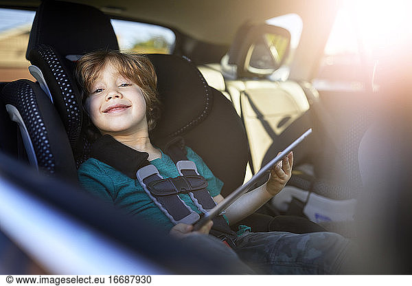 Portrait of smiling boy using digital tablet while sitting at back seat in car