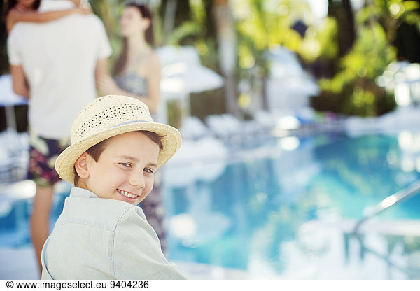 Portrait of smiling boy wearing sun hat sitting by swimming pool