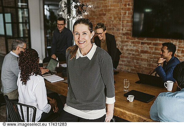 Portrait of smiling business professional standing while colleagues discussing in background