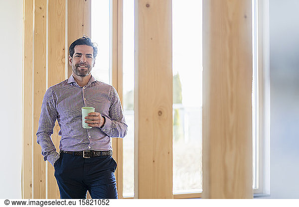 Portrait of smiling businessman holding cup in wooden open-plan office