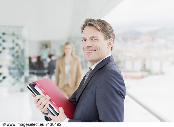 Portrait of smiling businessman holding paperwork in corridor