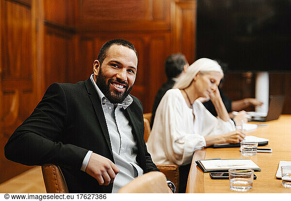 Portrait of smiling businessman sitting at conference table in board room during meeting