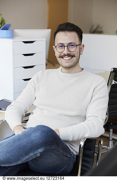 Portrait of smiling businessman sitting on chair at office