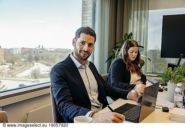 Portrait of smiling businessman sitting with colleague at desk in coworking office