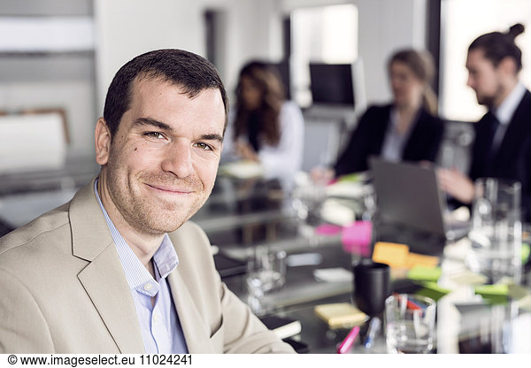 Portrait of smiling businessman sitting with colleagues at board room