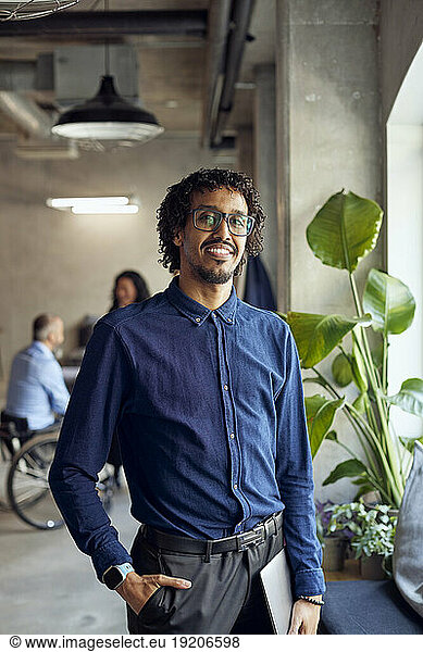 Portrait of smiling businessman standing with laptop at creative office