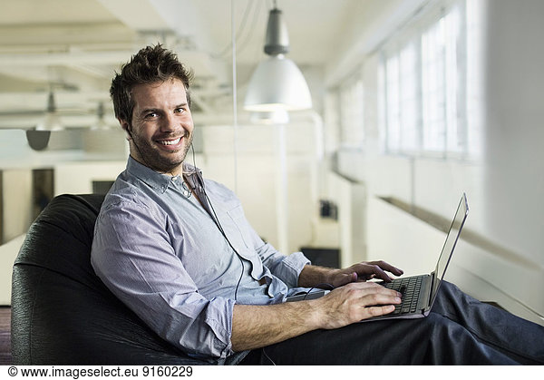 Portrait of smiling businessman using laptop while sitting on bean bag in office