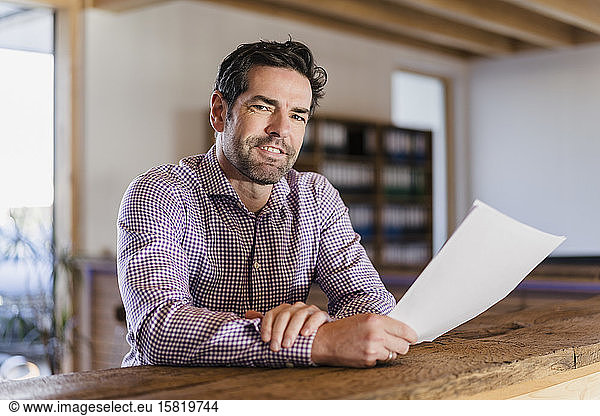Portrait of smiling businessman with document in wooden open-plan office