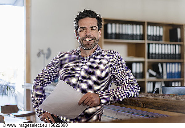 Portrait of smiling businessman with document in wooden open-plan office