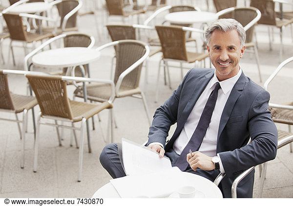 Portrait of smiling businessman with paperwork at sidewalk cafe