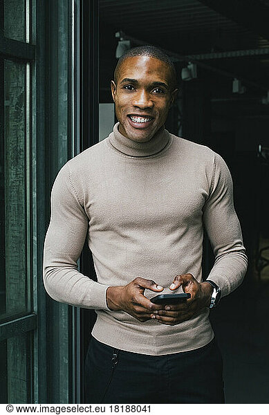 Portrait of smiling businessman with smart phone at doorway of office
