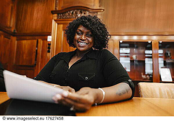 Portrait of smiling businesswoman holding contract document sitting at conference table in board room during meeting