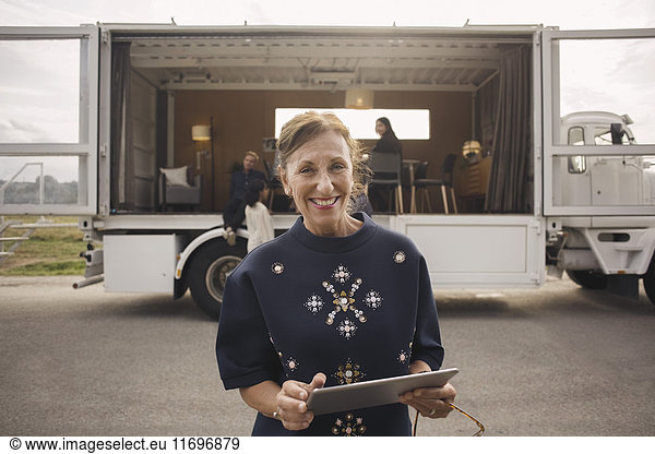 Portrait of smiling businesswoman holding digital tablet with colleagues and portable office truck in background