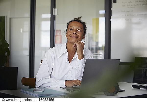 Portrait of smiling businesswoman sitting at desk in office looking at distance