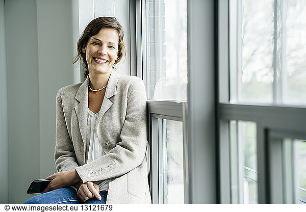 Portrait of smiling businesswoman sitting by window in office