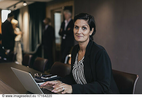 Portrait of smiling businesswoman sitting with laptop at conference table in board room