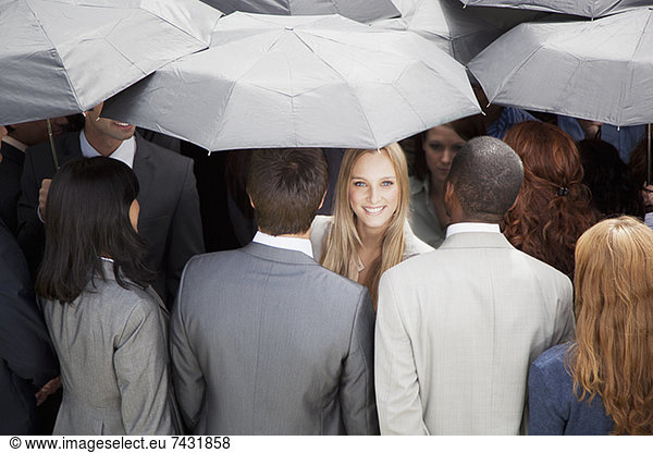 Portrait of smiling businesswoman surrounded by crowd with umbrellas