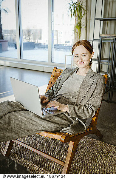 Portrait of smiling businesswoman using laptop while sitting in chair at office