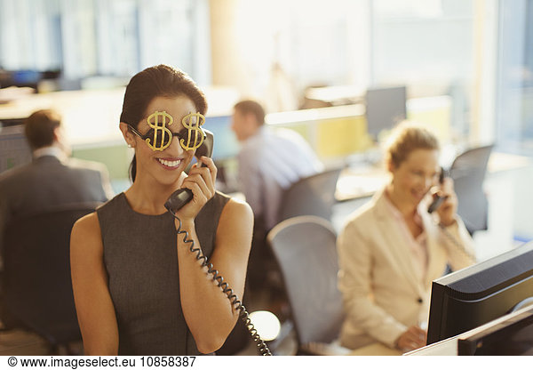 Portrait of smiling businesswoman wearing dollar sign sunglasses answering telephone in office