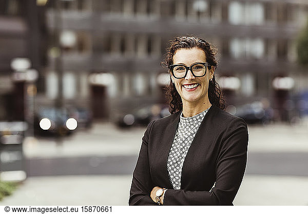 Portrait of smiling businesswoman with arms crossed standing outdoors