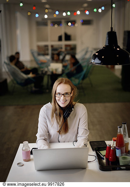 Portrait of smiling businesswoman working late on laptop in creative office