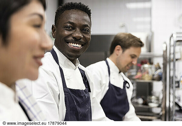 Portrait of smiling chef amidst colleagues working in kitchen at restaurant