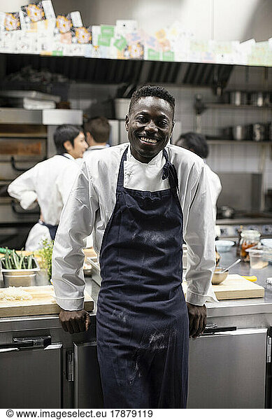 Portrait of smiling chef standing by kitchen counter at restaurant