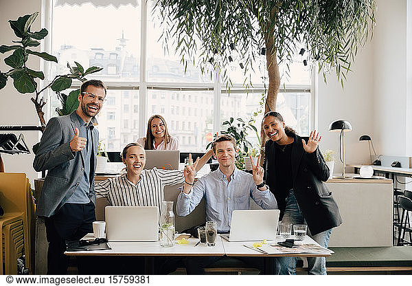 Portrait of smiling colleagues with laptops gesturing at desk in coworking space