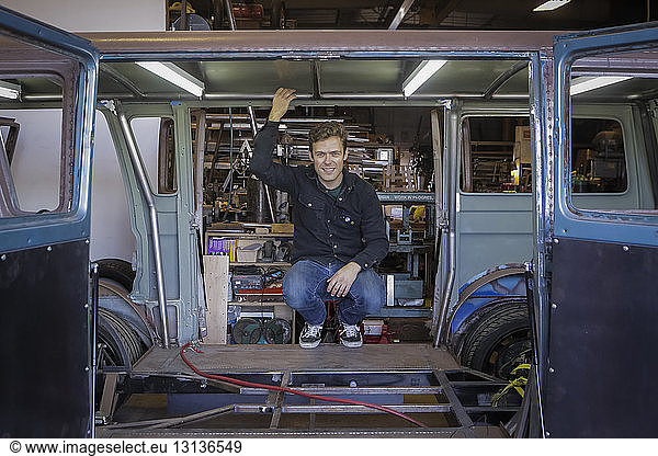 Portrait of smiling confident engineer crouching in damaged van at factory