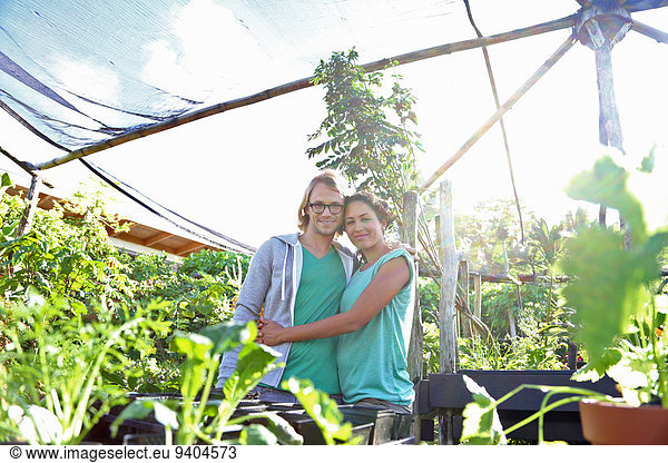 Portrait of smiling couple embracing in greenhouse  seedlings in foreground