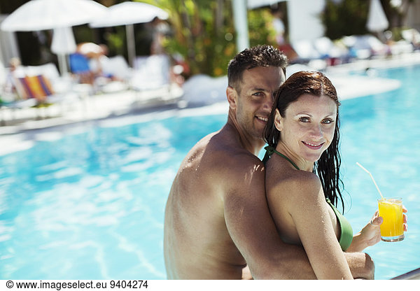 Portrait of smiling couple sitting by resort swimming pool