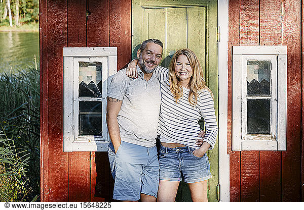 Portrait of smiling couple standing with arms around against door at log cabin