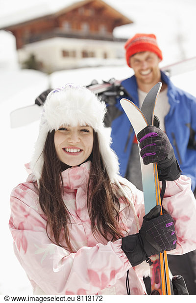 Portrait of smiling couple with skis outside cabin