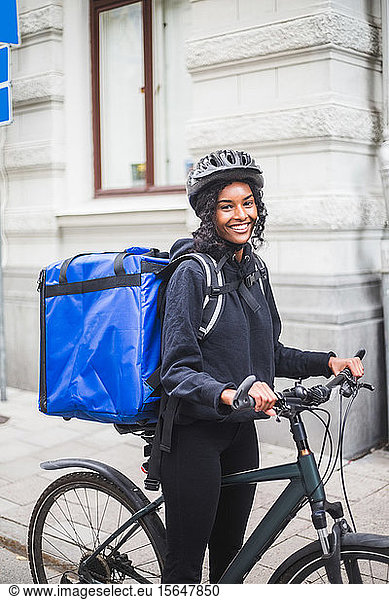 Portrait of smiling delivery woman with bicycle in city